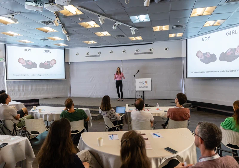 Boglarka presenting in front of a screen while audiance can be seen from behind watching the presentation.