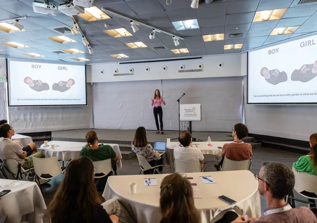Boglarka presenting in front of a screen while audiance can be seen from behind watching the presentation.