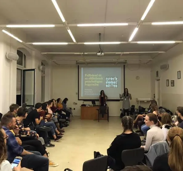 Boglarka presenting in a large room with students sitting in a circle around her.