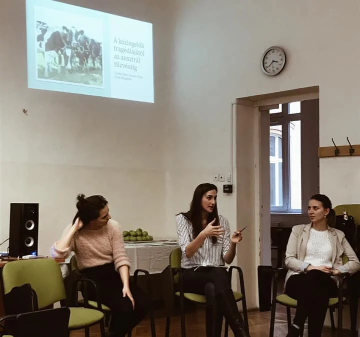 Boglarka and two people sitting in a room discussing a topic with a presentation projected to the wall in the background.