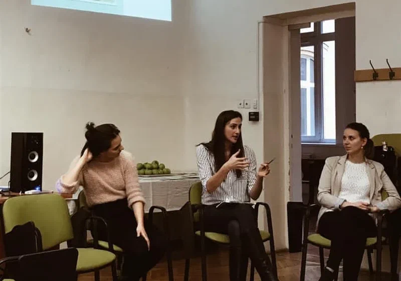 Boglarka and two people sitting in a room discussing a topic with a presentation projected to the wall in the background.